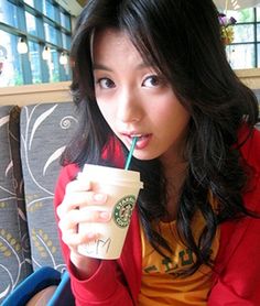 a woman sitting on a couch drinking from a starbucks cup with a straw in her mouth