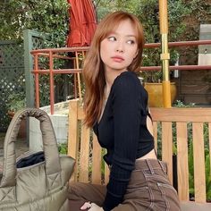 a young woman sitting on a bench with an umbrella in the background and a purse behind her