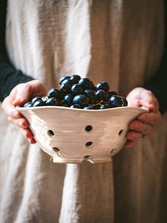 a person holding a white bowl filled with black olives