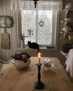 a cat sitting on the window sill next to a table with plates and cups