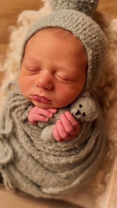 a newborn baby wearing a knitted hat and holding a teddy bear in its arms