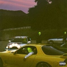 a yellow sports car with green alien heads on it's windshield and two people in the background