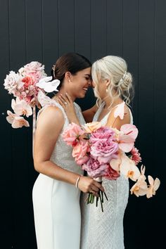 two brides hugging each other with flowers in their hair and bouquets on their heads