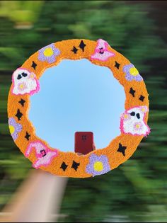 a hand holding up a decorated orange and pink wreath with sheeps in the center