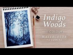 the indigo woods watercolor book is next to a pencil and eraser on a wooden table