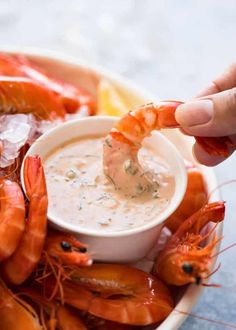 a person dipping shrimp into a bowl of dip with lemon wedges on the side