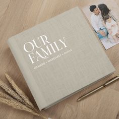 a family book sitting on top of a wooden table next to a pen and two photos