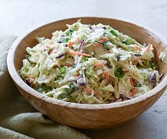 a wooden bowl filled with coleslaw salad on top of a green cloth covered table