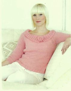 a woman sitting on top of a white couch wearing a pink sweater and white pants