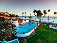 an aerial view of a swimming pool surrounded by palm trees and the ocean in the background