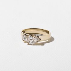 a three stone diamond ring on a white surface, with the center setting in yellow gold