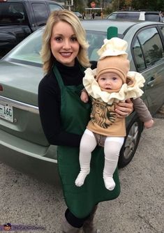 a woman holding a baby in her arms while standing next to a green car and wearing a costume