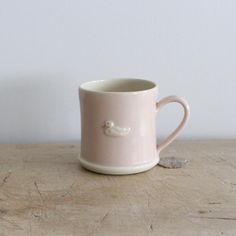 a pink coffee cup sitting on top of a wooden table next to a white wall