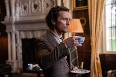 a man in a suit is holding a cup and saucer while looking off into the distance