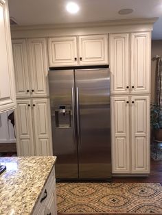 a stainless steel refrigerator in a kitchen with white cabinetry and granite counter tops, along with an area rug