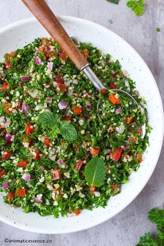 a white bowl filled with green salad next to a wooden spoon on top of a table