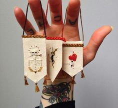 someone is holding up their hand decorated with small pieces of fabric and thread, which are hanging from strings