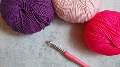 three balls of yarn next to a crochet hook on a gray table top