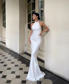 a woman in a white dress leaning against a wall