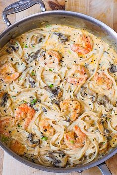 a pan filled with pasta and shrimp on top of a wooden table