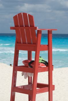 a red chair sitting on top of a sandy beach next to the ocean with a life preserver