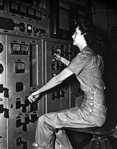 a woman sitting on top of a control panel in an industrial building with lots of switches