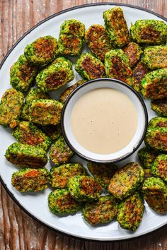 a white plate topped with broccoli covered in sauce next to a small bowl