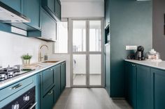 a narrow kitchen with blue cabinets and white counter tops, along with an open door leading to the outside