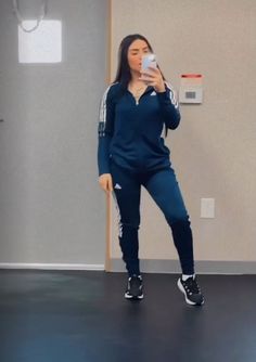 a woman taking a selfie with her cell phone in an empty room while wearing adidas