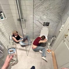 two people sitting on the floor in a bathroom with their backs to each other and one person taking a photo