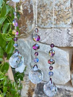 three different colored beads hanging from a chain next to a rock and green plant in front of a stone wall