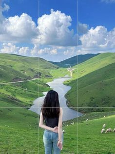 a woman standing on top of a lush green hillside next to a lake and sheep