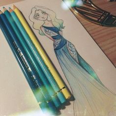 some colored pencils are sitting on top of a paper with a drawing of a mermaid