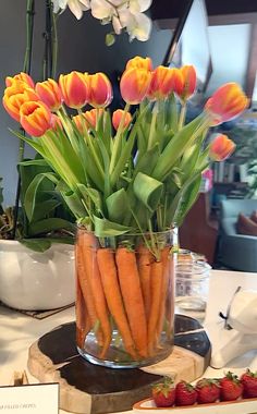 carrots and tulips are arranged in a glass vase