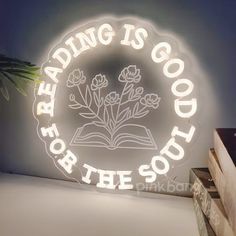 reading is good for the soul neon sign with book and plant on table next to stack of books