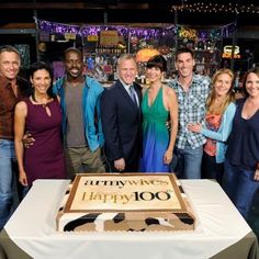 a group of people standing around a table with a cake on it that says happy birthday