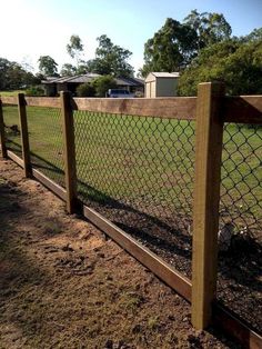 a fence that is next to a field with grass and dirt on the ground in front of it