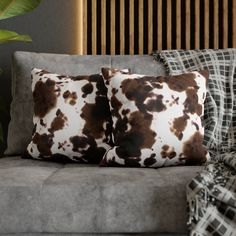 two brown and white pillows sitting on top of a gray couch next to a plant