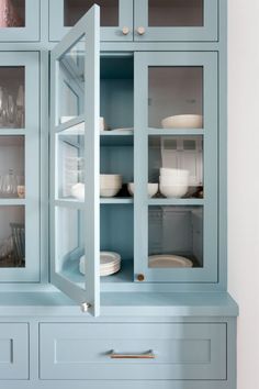 a blue china cabinet with glass doors and dishes on it's shelves in a kitchen