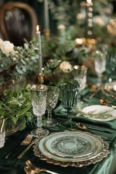 the table is set with green and gold plates, silverware, greenery and candles