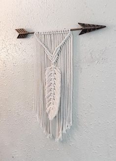 a wall hanging with an arrow and two feathers on it's side, against a white wall