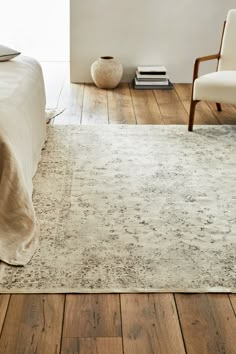 a white bed sitting on top of a wooden floor next to a chair and table