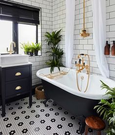 a black and white tiled bathroom with a claw foot bathtub, potted houseplant, and gold faucet