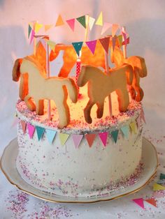 a birthday cake decorated with horses and bunting streamers on a white tablecloth