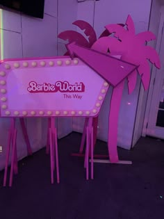 there is a sign that says barbie world the way in front of a wall with palm trees