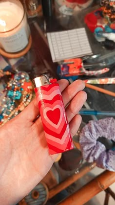 a hand holding a red lighter with a heart on it in front of a glass table