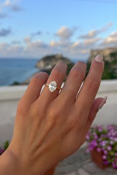 a woman's hand with a ring on her finger and flowers in the background