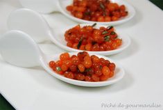 three white spoons filled with tomatoes on top of a table