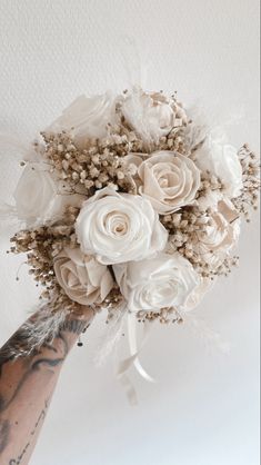 a bride's bouquet with white roses and feathers on her arm is held up in the air