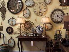 many clocks are hanging on the wall above a table with lamp shades and lampshades